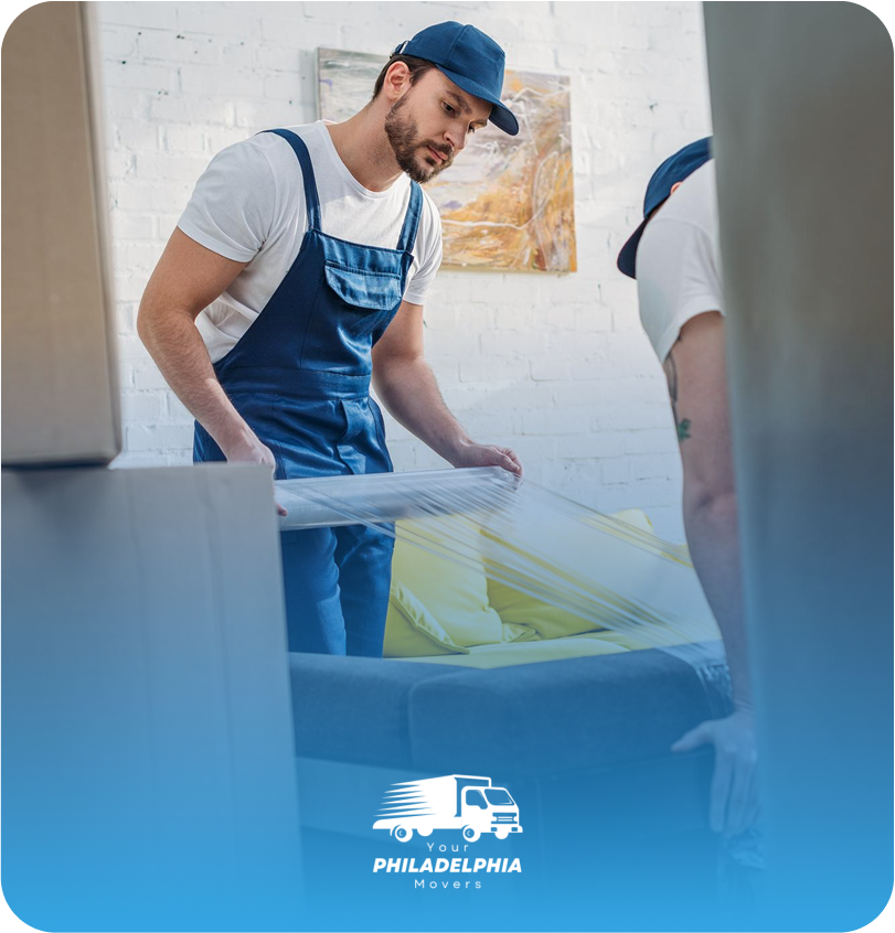 Professional movers from Your Philadelphia Movers carefully wrapping a couch with protective plastic for safe transport.